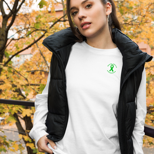 A woman stands outdoors in autumn, wearing the You Are Not Alone Mental Health Awareness Unisex Long Sleeve Tee with a green ribbon and 988 crisis hotline text, supporting mental health awareness as she gazes at the camera.