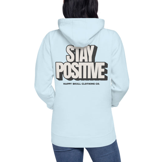 A person wears the Stay Positive Unisex Hoodie in light blue, displaying STAY POSITIVE and HAPPY SKULL CLOTHING CO. in bold black and cream on the back. Paired with jeans, it subtly promotes self-care and mental well-being through its uplifting message.