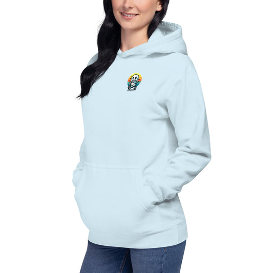 A woman in a light blue Stay Positive Unisex Hoodie with a small colorful chest graphic stands confidently, hands in pockets. Her long dark hair cascades as she smiles warmly, embodying self-care and mental well-being against a plain white backdrop.