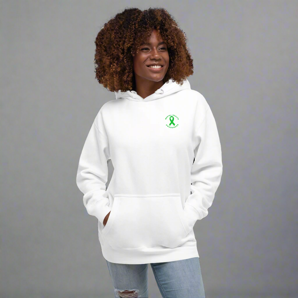 A woman with curly hair wears the You Are Not Alone Mental Health Awareness Hoodie—a white hoodie with a green ribbon and text on the left chest. She smiles, hands in pockets, standing against a black background.