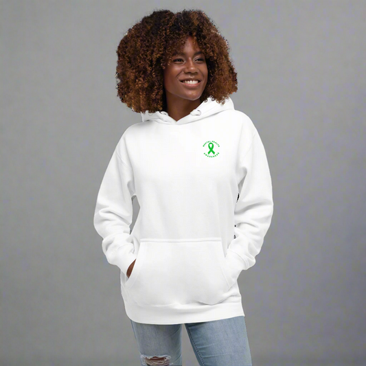 A woman with curly hair wears the You Are Not Alone Mental Health Awareness Hoodie—a white hoodie with a green ribbon and text on the left chest. She smiles, hands in pockets, standing against a black background.