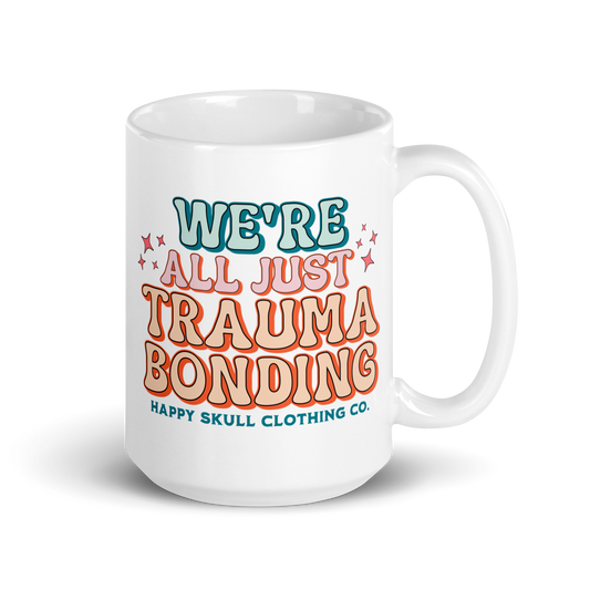 The We’re All Just Trauma Bonding - 15oz Coffee Mug features colorful text with decorative stars and “Happy Skull Clothing Co.” in teal and orange—an ideal mug for your healing journey.