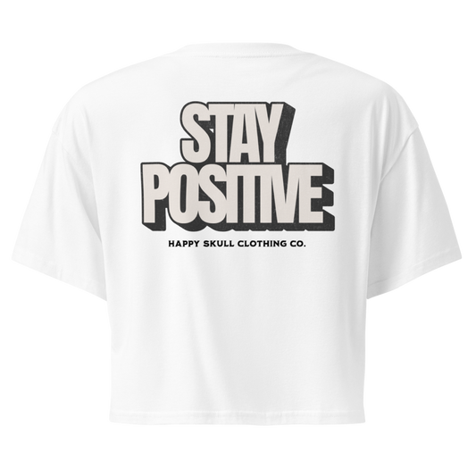 White crop top with STAY POSITIVE in bold, black 3D-style text on the back, elegantly embodying the spirit of Happy Skull Clothing Co.